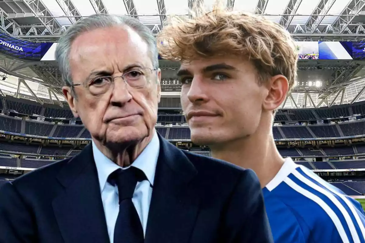 Dos personas en primer plano dentro de un estadio de fútbol una de ellas lleva traje y la otra viste un uniforme deportivo azul con blanco