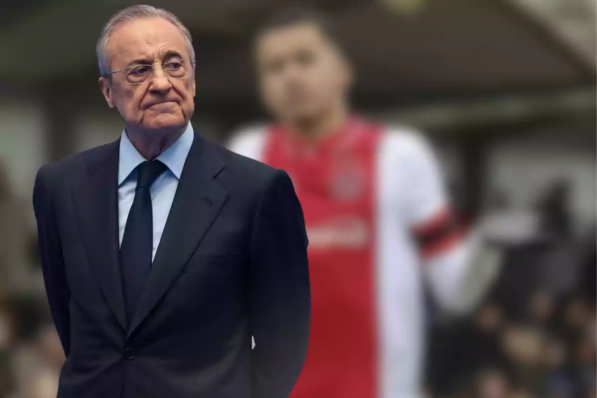 Man in a dark suit with a serious expression in the foreground and a blurred figure of a player in the background