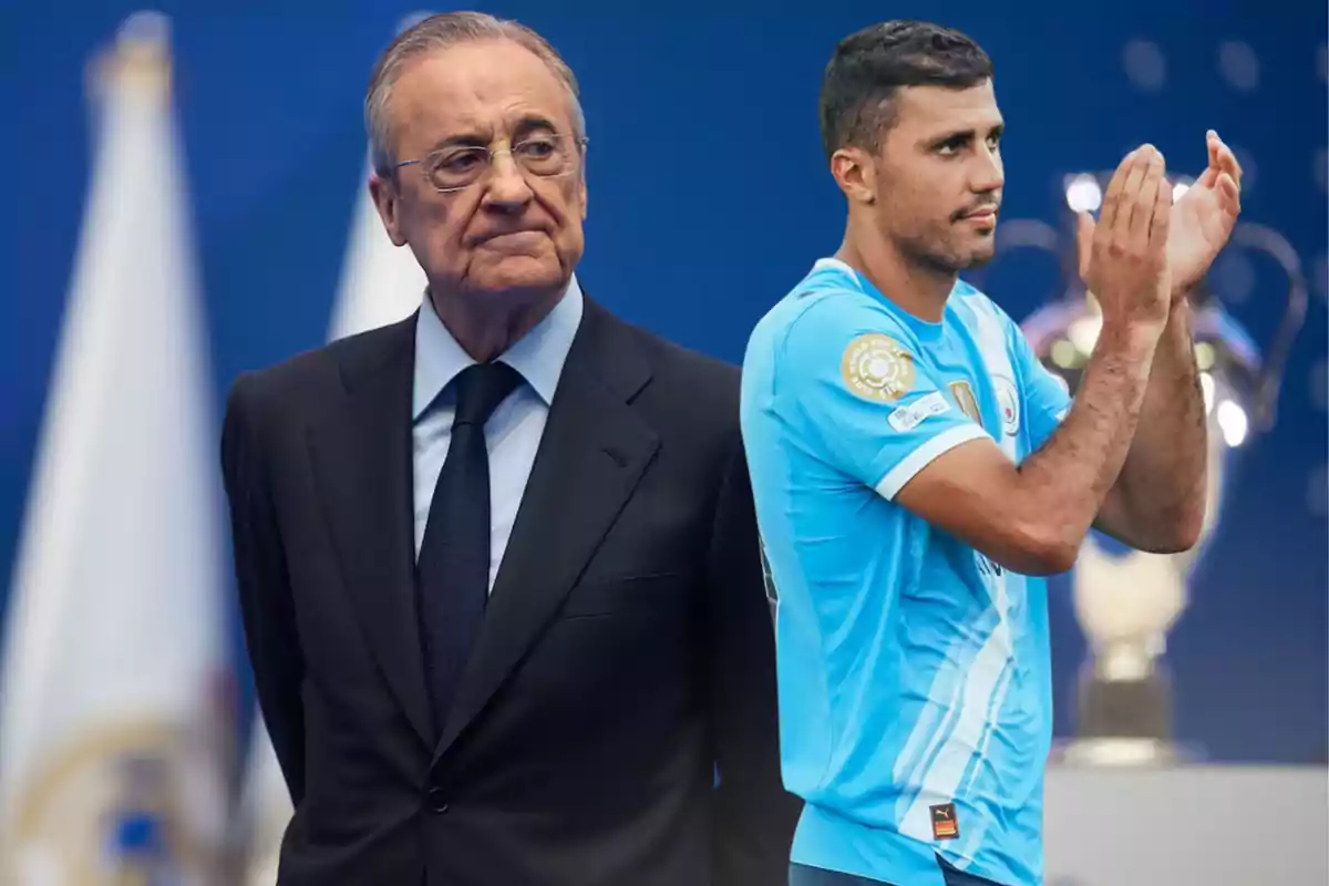 Un hombre de traje oscuro está de pie junto a un futbolista con uniforme celeste que aplaude, al fondo se observa un trofeo desenfocado.
