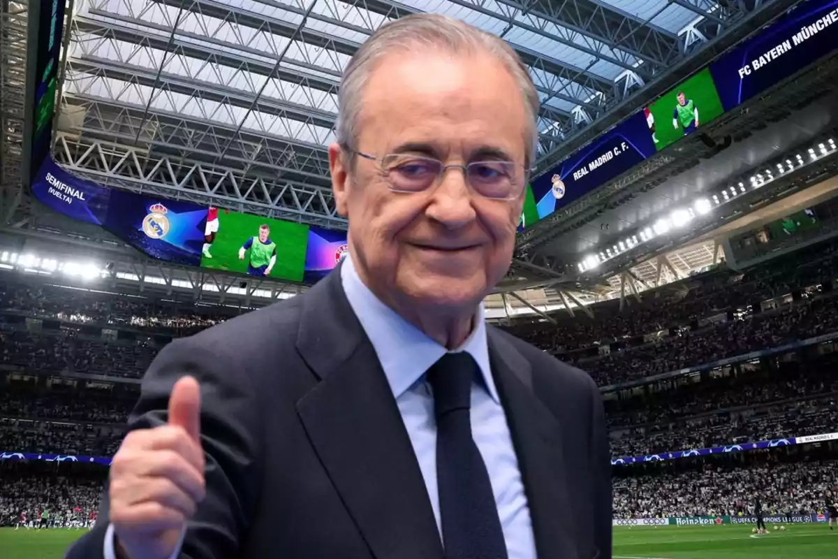 Hombre de traje sonriente levantando el pulgar en un estadio de fútbol lleno de aficionados