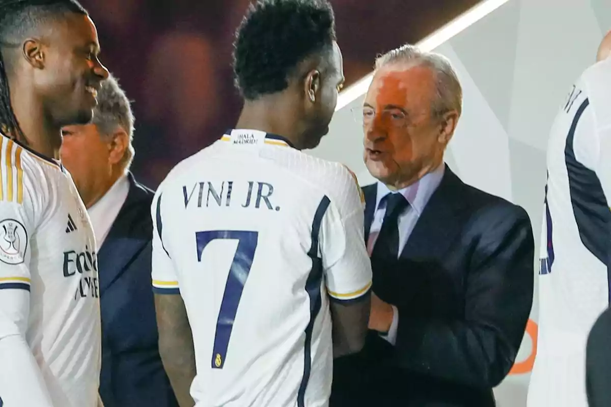 A Real Madrid player wearing the number 7 jersey greets a man in a suit during a ceremony while other players watch. A Real Madrid player wearing the number 7 jersey greets a man in a suit during a ceremony while other players watch.