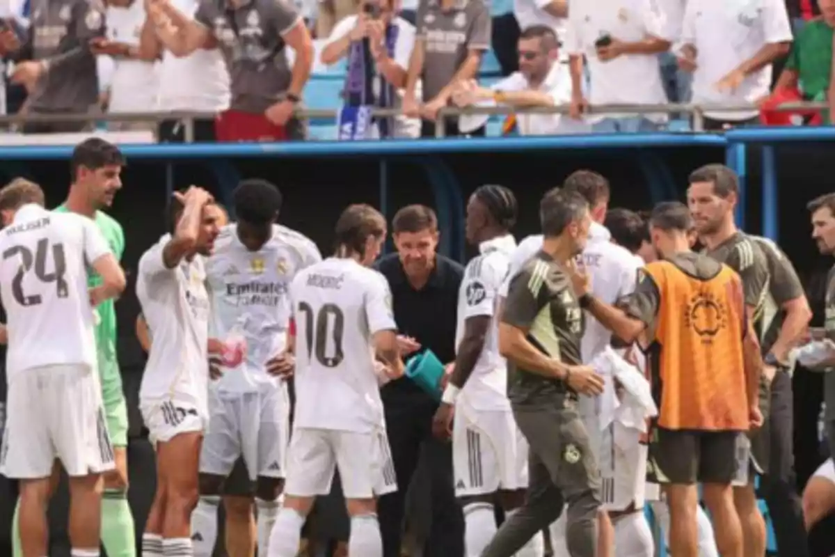 Real Madrid players and coaching staff gathered on the sideline during a match with fans watching from the stands Real Madrid players and coaching staff gathered on the sideline during a match with fans watching from the stands