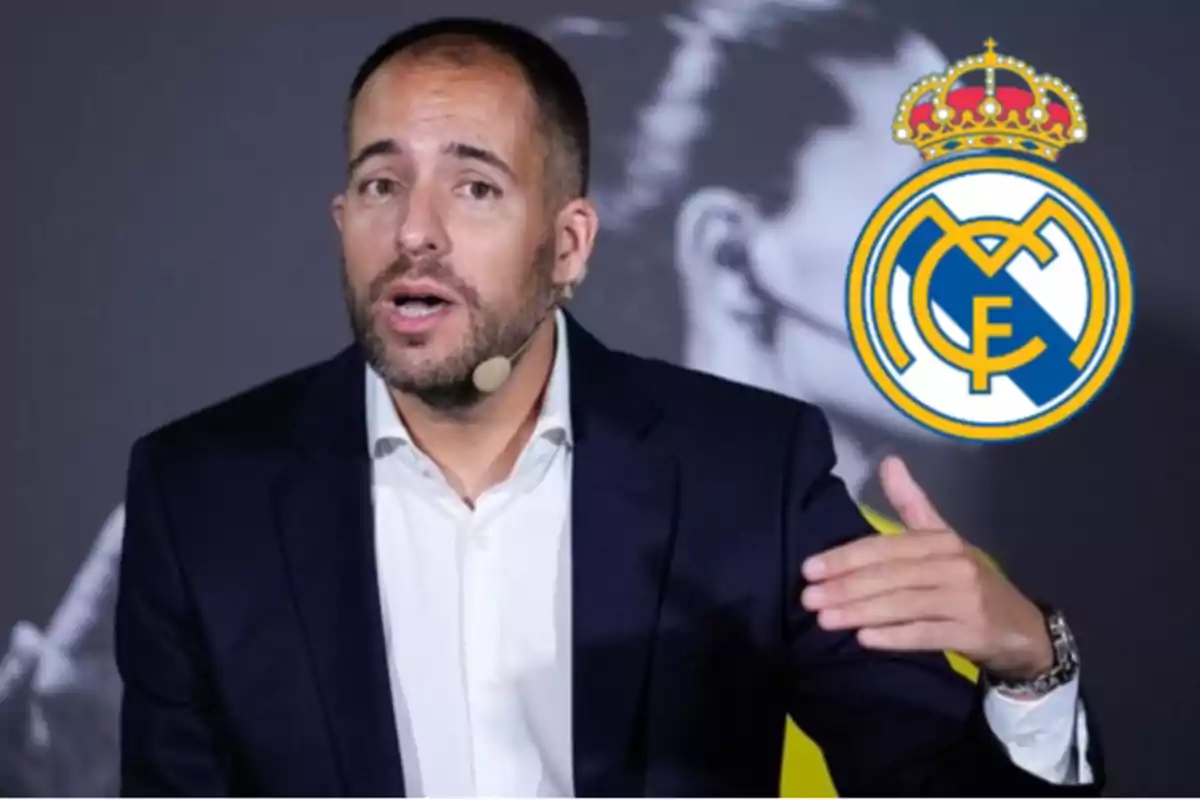 Man with a headset microphone speaking and gesturing with his hand, wearing a dark suit and white jersey, with the Real Madrid crest visible in the background.