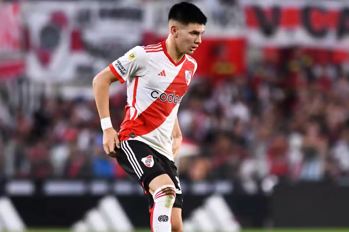 Jugador de River Plate con uniforme blanco y rojo en pleno partido de fútbol en un estadio lleno de aficionados Jugador de River Plate con uniforme blanco y rojo en pleno partido de fútbol en un estadio lleno de aficionados