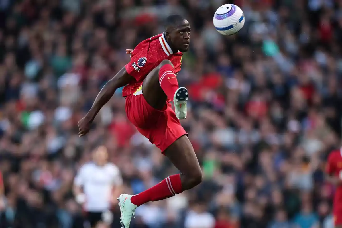 Soccer player in a red uniform jumps to hit the ball in a stadium full of spectators Soccer player in a red uniform jumps to hit the ball in a stadium full of spectators