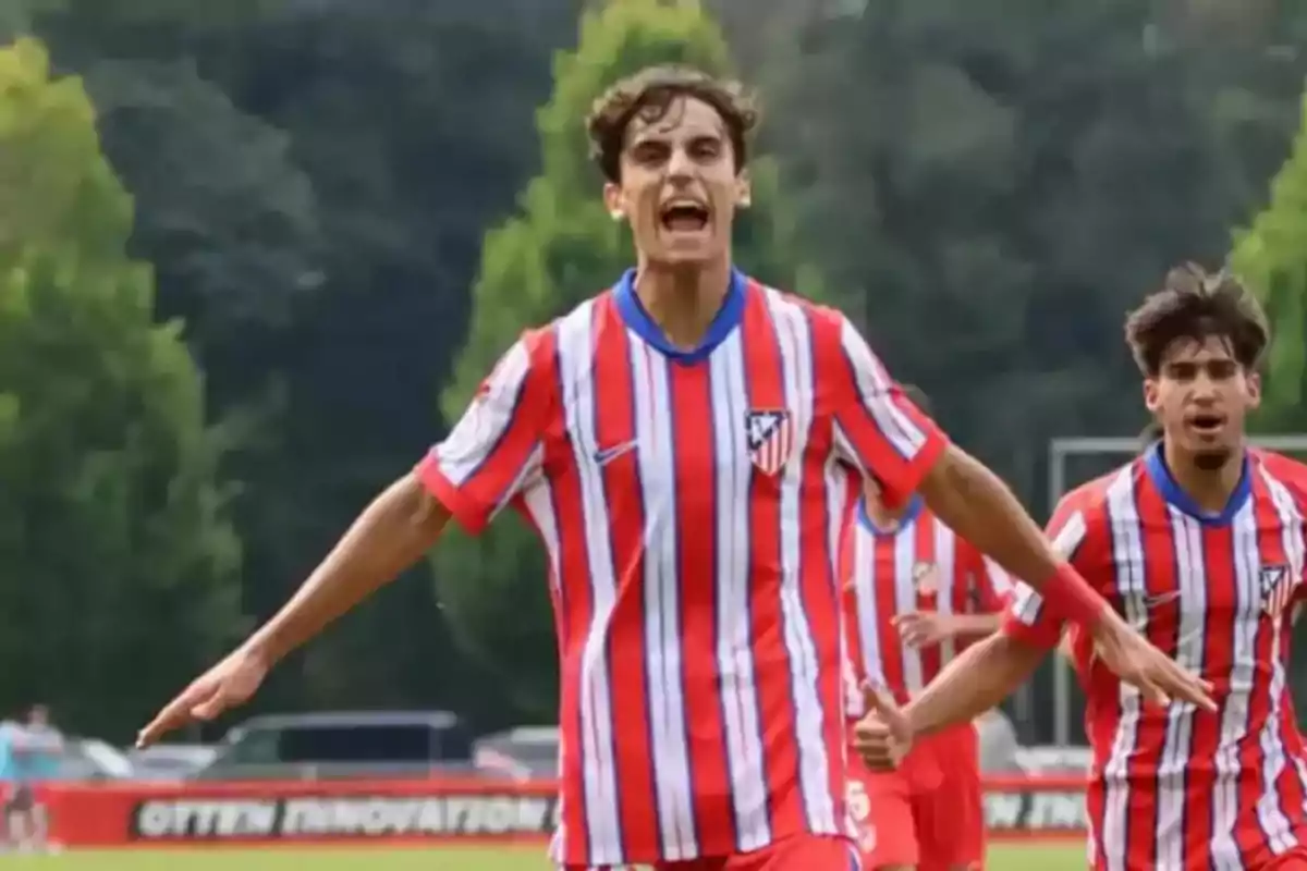 Jugador de fútbol celebrando un gol con los brazos extendidos mientras viste el uniforme rojiblanco del Atlético de Madrid en un campo al aire libre Jugador de fútbol celebrando un gol con los brazos extendidos mientras viste el uniforme rojiblanco del Atlético de Madrid en un campo al aire libre