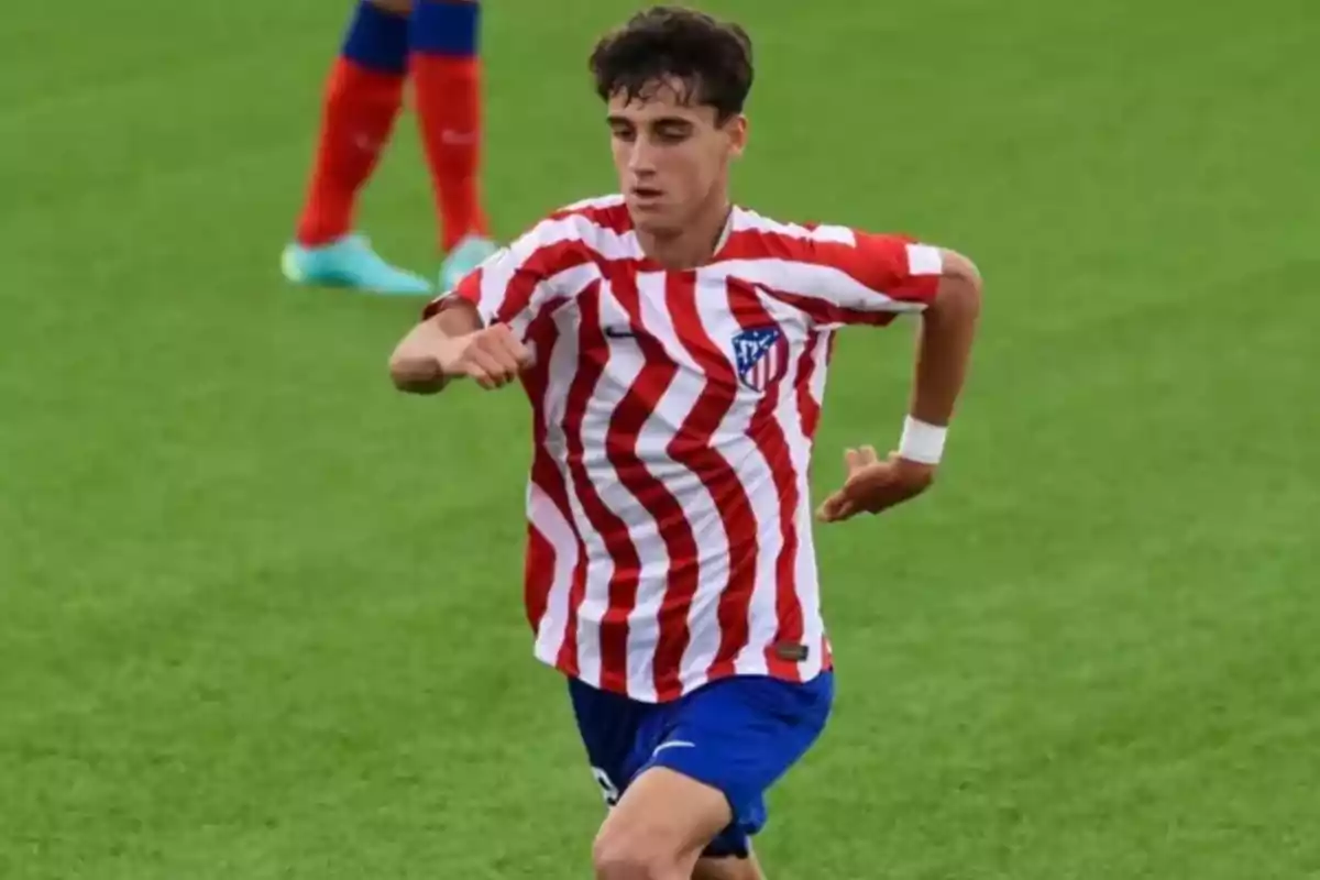 Joven futbolista con uniforme rojiblanco y pantalones azules corriendo en un campo de césped Joven futbolista con uniforme rojiblanco y pantalones azules corriendo en un campo de césped