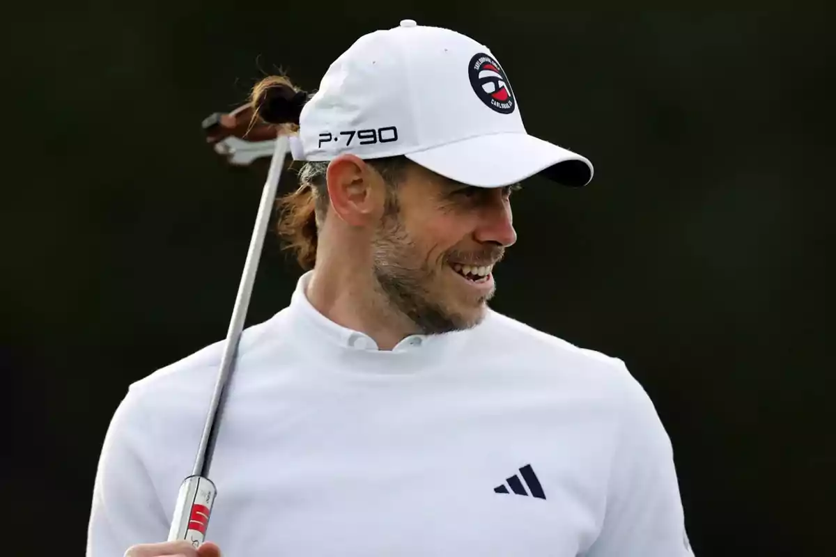 Smiling man wearing a white cap and sports jersey holding a golf club over his shoulder