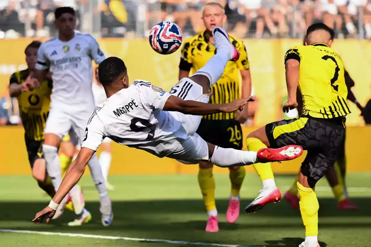 Soccer player in a white uniform performs a bicycle kick in a match against a team in yellow and black uniforms while several players watch the play. Soccer player in a white uniform performs a bicycle kick in a match against a team in yellow and black uniforms while several players watch the play.