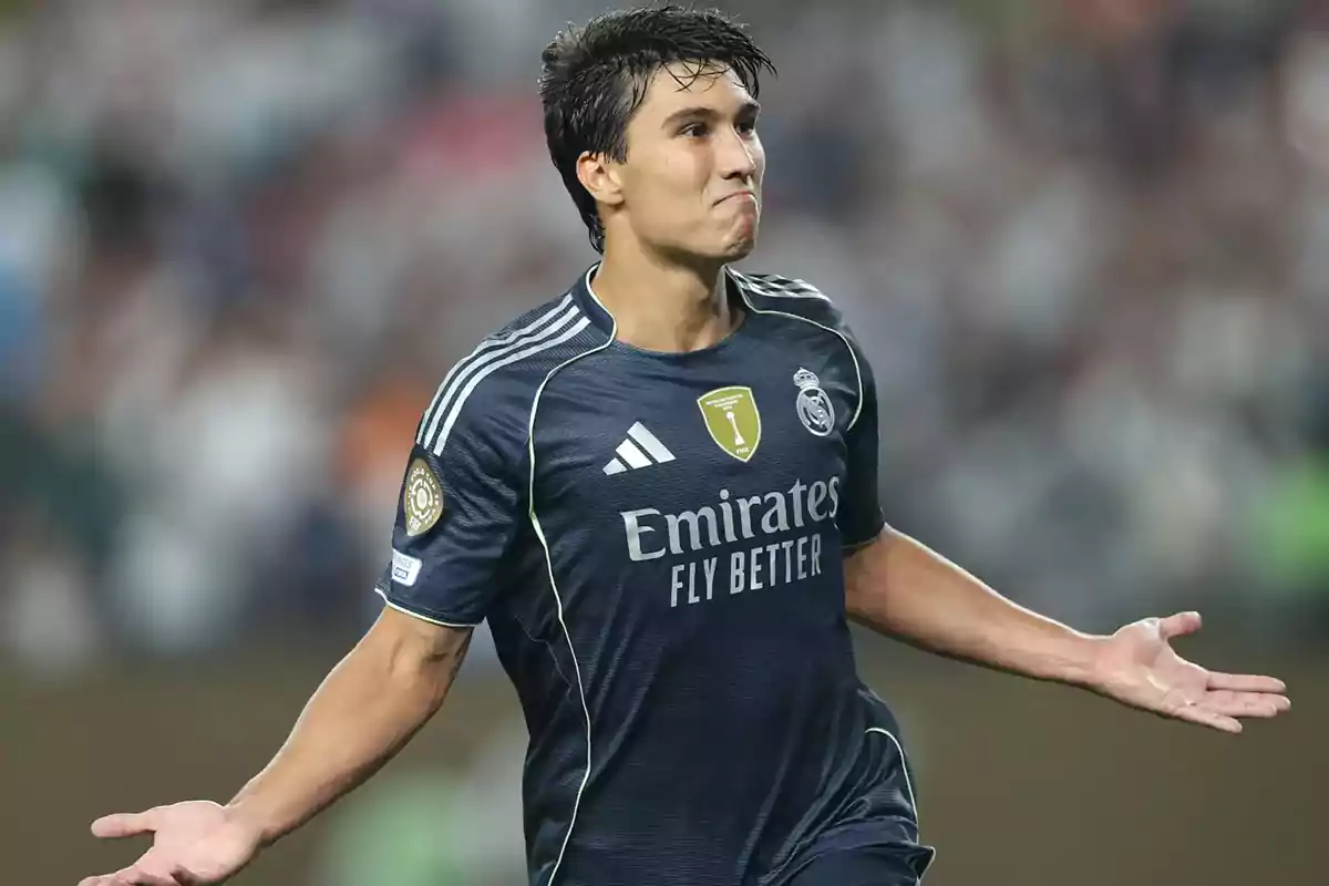Futbolista con uniforme oscuro del Real Madrid celebrando en el campo con los brazos extendidos y expresión de satisfacción Futbolista con uniforme oscuro del Real Madrid celebrando en el campo con los brazos extendidos y expresión de satisfacción
