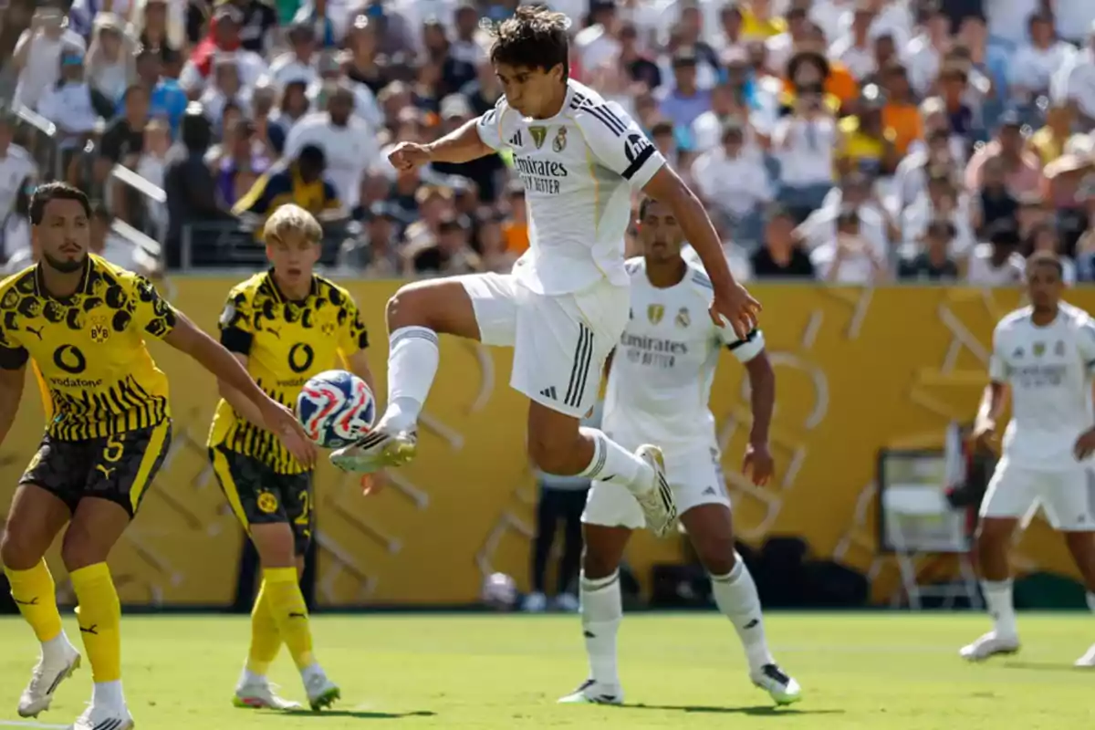 Un jugador del Real Madrid controla el balón en el aire durante un partido contra el Borussia Dortmund mientras varios jugadores observan la jugada en el campo. Un jugador del Real Madrid controla el balón en el aire durante un partido contra el Borussia Dortmund mientras varios jugadores observan la jugada en el campo.