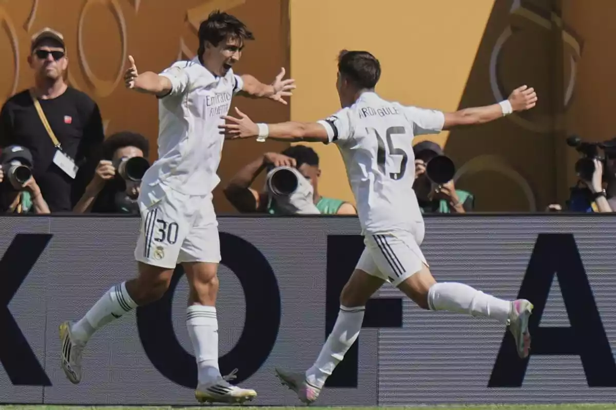 Dos futbolistas del Real Madrid celebran un gol abrazándose en el campo mientras varios fotógrafos capturan el momento desde el fondo Dos futbolistas del Real Madrid celebran un gol abrazándose en el campo mientras varios fotógrafos capturan el momento desde el fondo