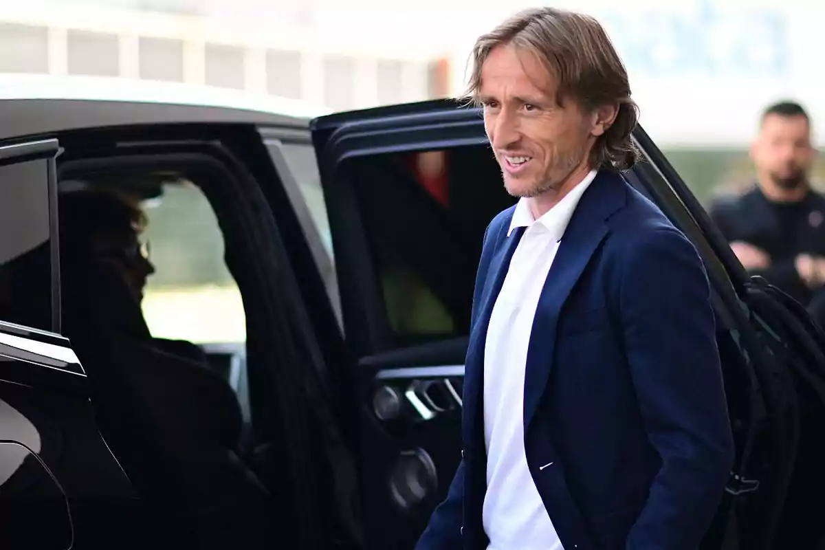 Hombre con chaqueta azul y camisa blanca saliendo de un automóvil negro