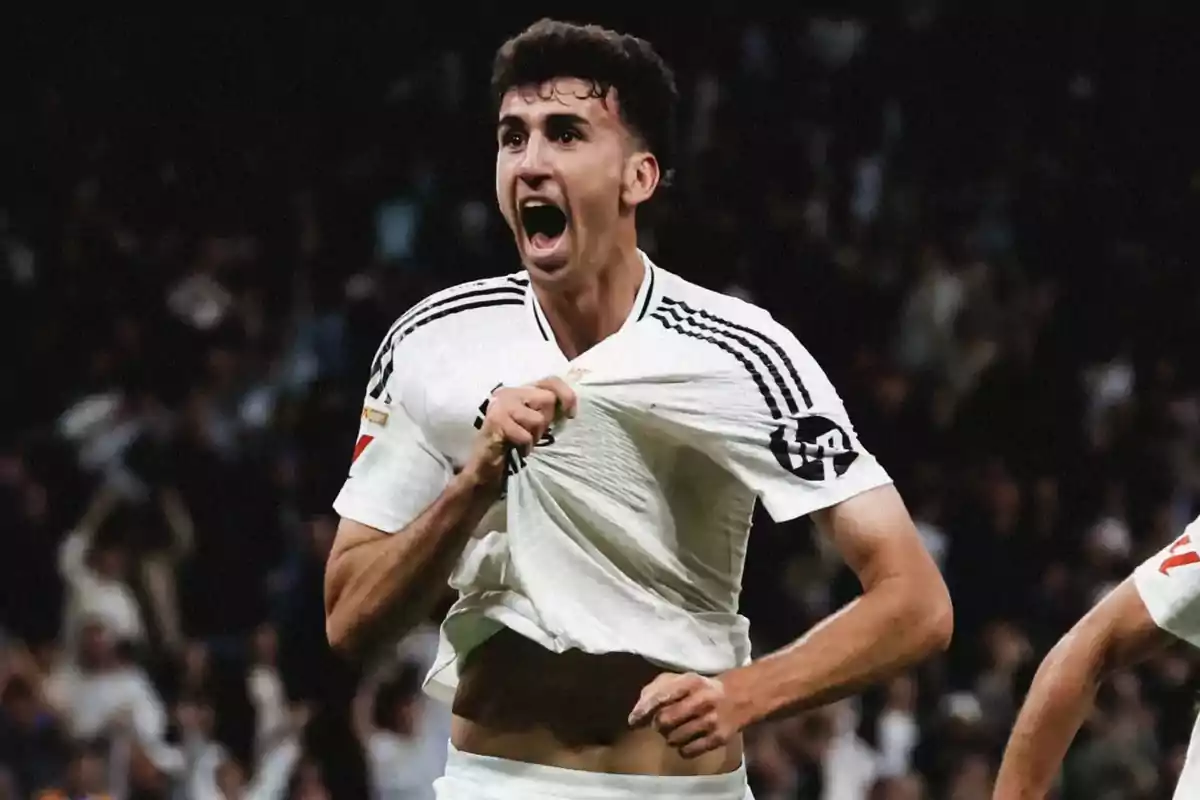 Futbolista celebrando un gol con emoción mientras sostiene su camiseta blanca frente a una multitud en el estadio Futbolista celebrando un gol con emoción mientras sostiene su camiseta blanca frente a una multitud en el estadio