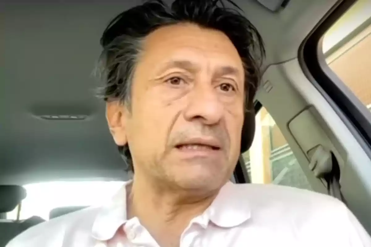 Hombre de mediana edad con cabello oscuro y camisa clara sentado dentro de un automóvil mirando hacia el frente