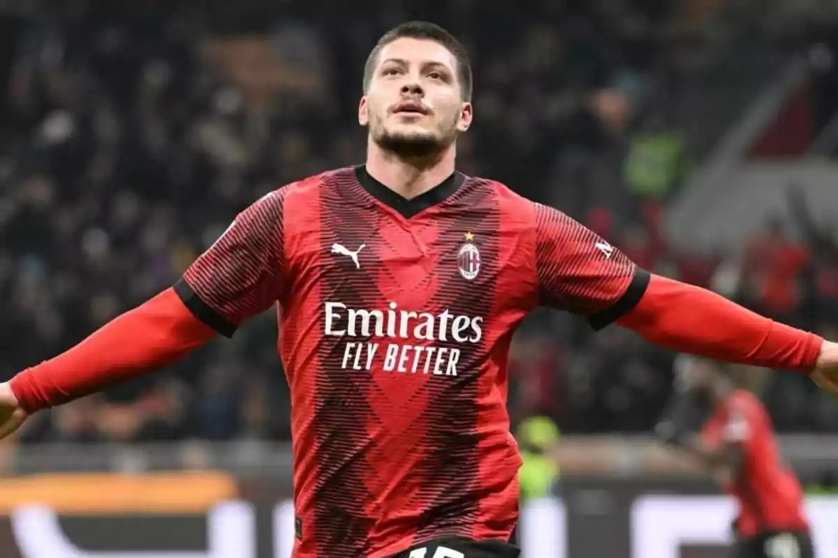 Futbolista con uniforme rojo y negro del AC Milan celebrando un gol con los brazos extendidos en un estadio lleno de espectadores