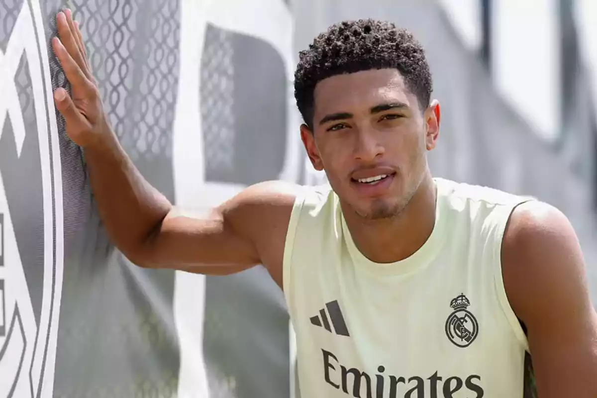Young player wearing a Real Madrid training jersey leaning against a club banner and smiling at the camera Young player wearing a Real Madrid training jersey leaning against a club banner and smiling at the camera