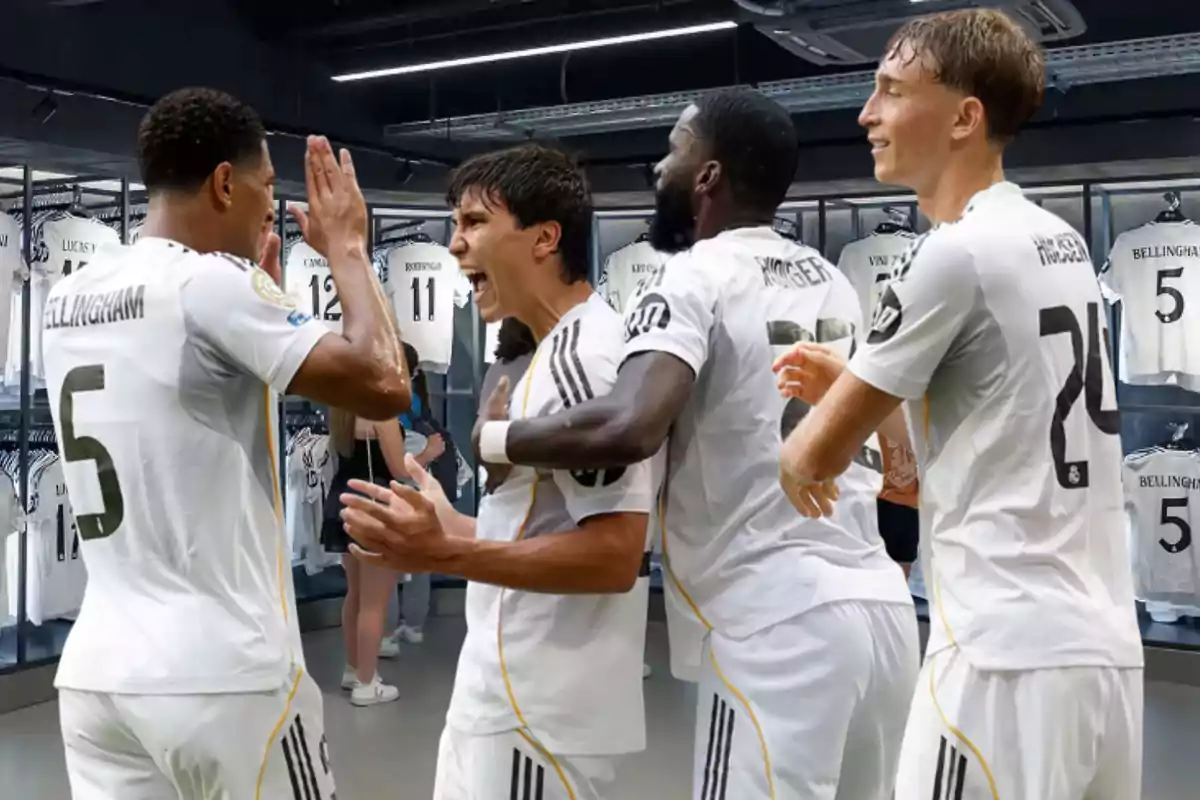 Cuatro futbolistas del Real Madrid celebran juntos en un vestuario rodeados de camisetas blancas colgadas en el fondo