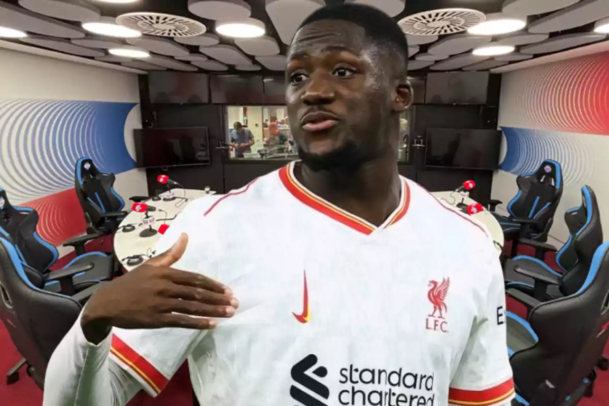 A player wearing a white Liverpool jersey is in the foreground inside a modern recording studio with gaming chairs and microphones.