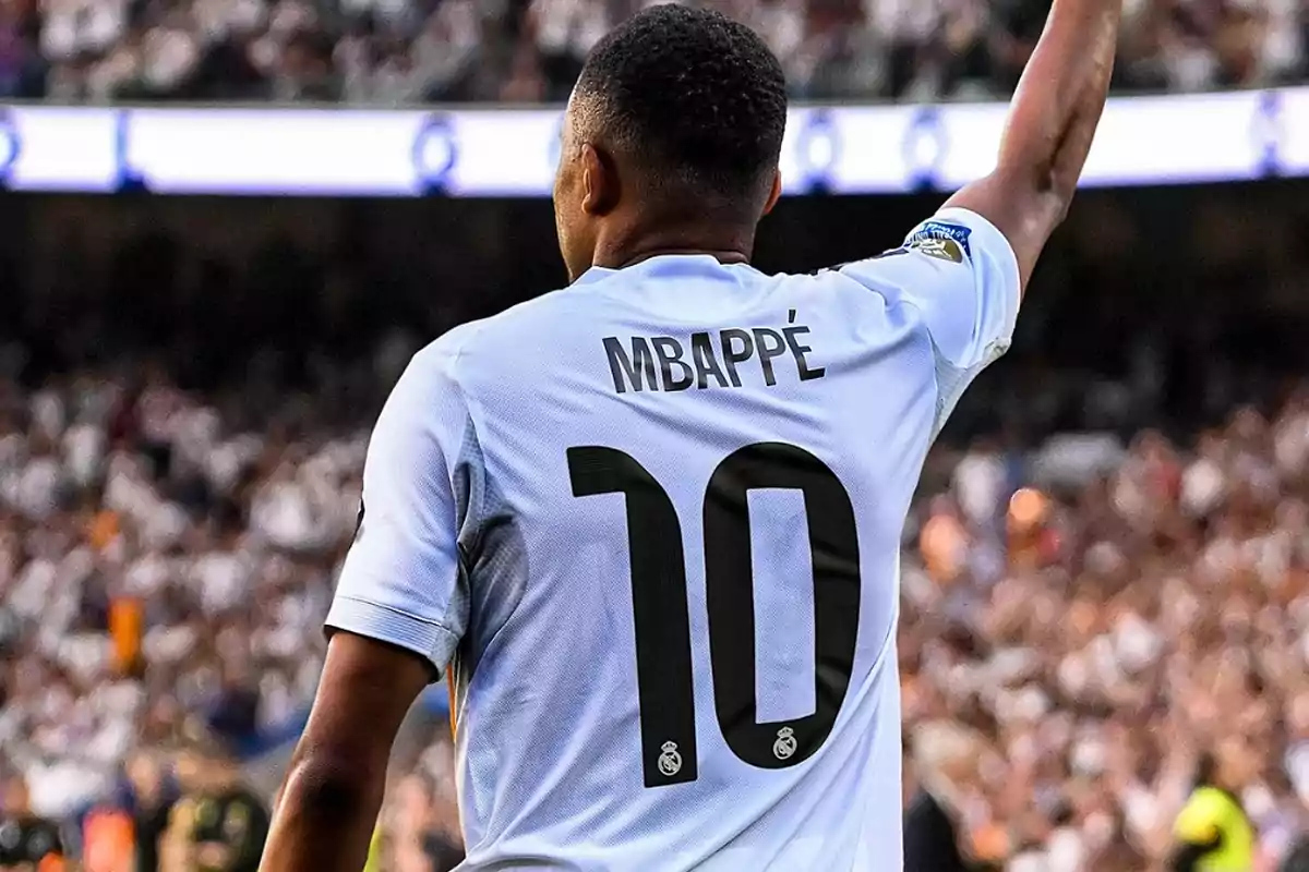 Futbolista con la camiseta número 10 y el nombre Mbappé levantando el brazo en un estadio lleno de aficionados Futbolista con la camiseta número 10 y el nombre Mbappé levantando el brazo en un estadio lleno de aficionados