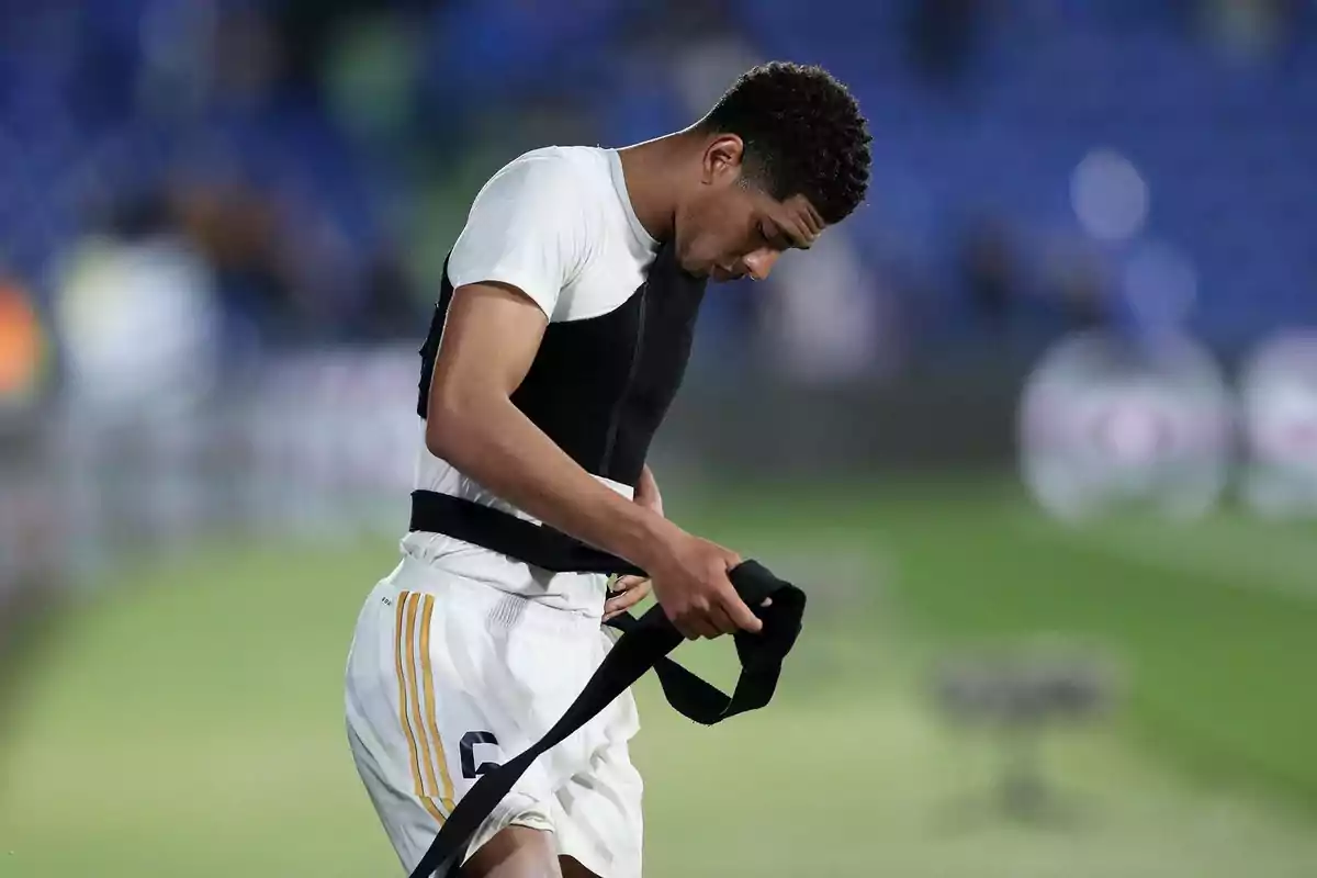 A player wearing a white jersey and white shorts is holding a black garment in a soccer stadium. A player wearing a white jersey and white shorts is holding a black garment in a soccer stadium.