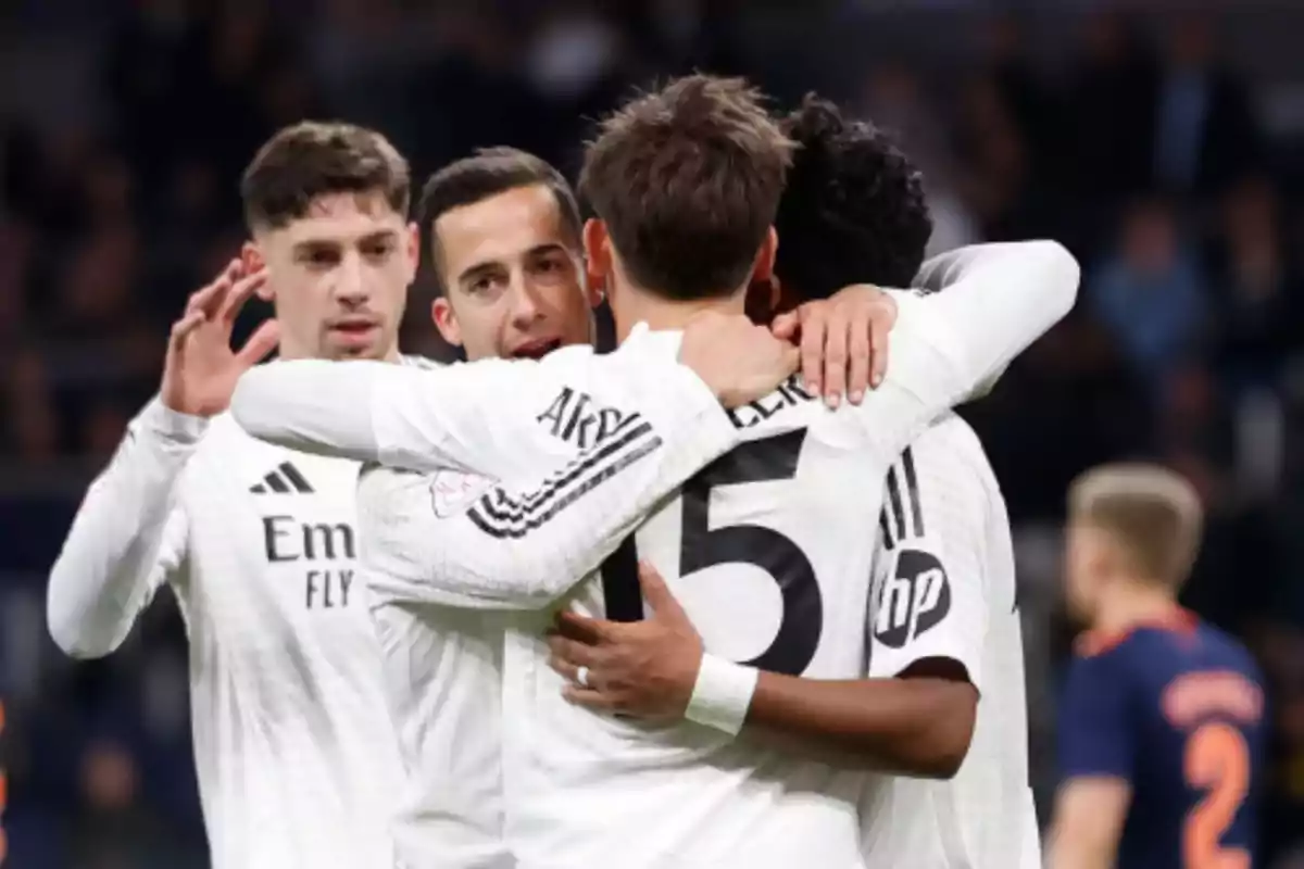Jugadores de fútbol con uniforme blanco celebran un gol abrazándose en el campo durante un partido Jugadores de fútbol con uniforme blanco celebran un gol abrazándose en el campo durante un partido