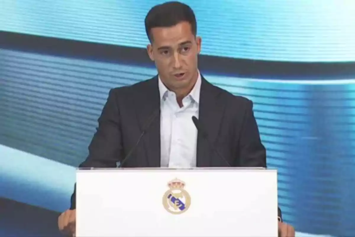 Hombre con traje oscuro hablando en un podio con el escudo del Real Madrid al frente y fondo azul