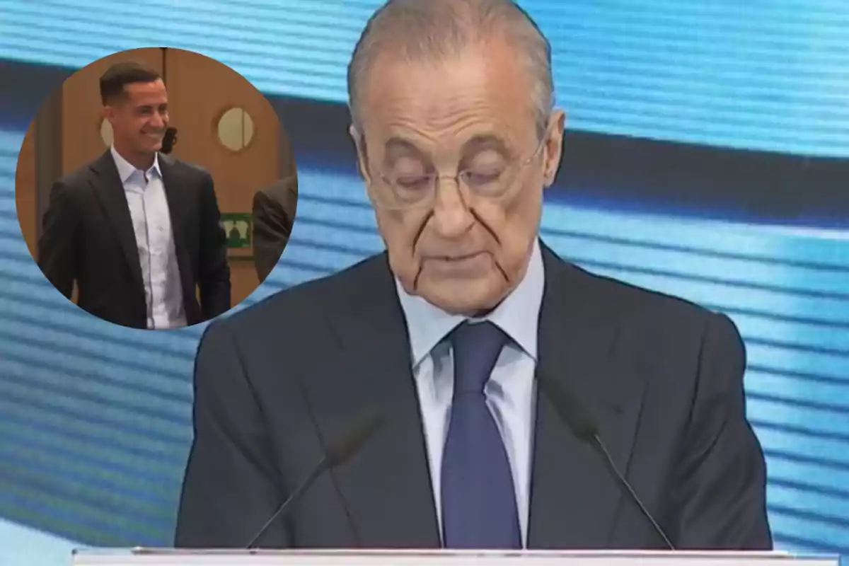 Older man with glasses and a suit speaking at a podium with a blue screen in the background and a box showing a smiling young man also dressed in a suit