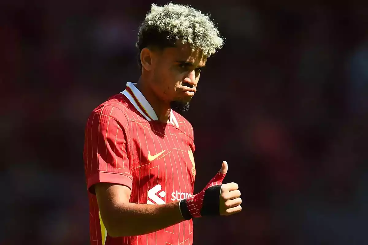 Futbolista con cabello rizado y teñido usando uniforme rojo de Liverpool haciendo gesto de aprobación con el pulgar arriba Futbolista con cabello rizado y teñido usando uniforme rojo de Liverpool haciendo gesto de aprobación con el pulgar arriba