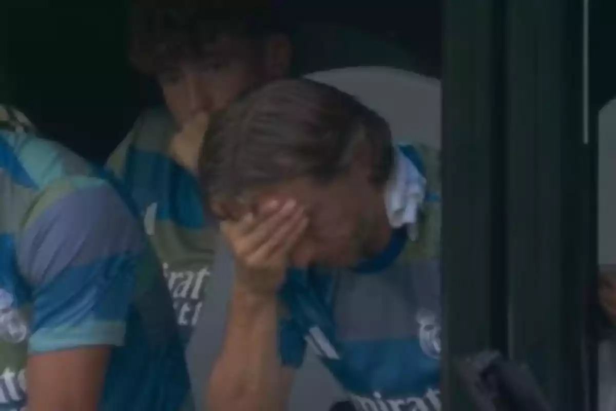 Un jugador de fútbol con uniforme de entrenamiento se cubre el rostro con la mano mostrando una expresión de frustración o tristeza mientras está sentado en la banca Un jugador de fútbol con uniforme de entrenamiento se cubre el rostro con la mano mostrando una expresión de frustración o tristeza mientras está sentado en la banca