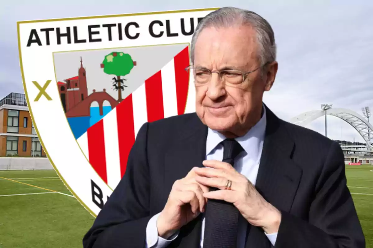 Hombre de traje con gafas frente al escudo del Athletic Club en un campo de fútbol