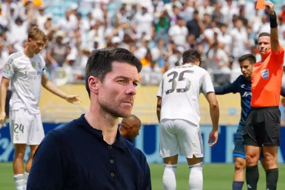 A soccer coach looks thoughtful in the foreground while in the background a referee shows a red card to a player during a match.
