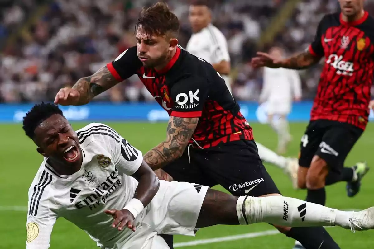 Un jugador del Real Madrid cae al césped con gesto de dolor mientras un futbolista del Mallorca lo empuja durante un partido de fútbol Un jugador del Real Madrid cae al césped con gesto de dolor mientras un futbolista del Mallorca lo empuja durante un partido de fútbol