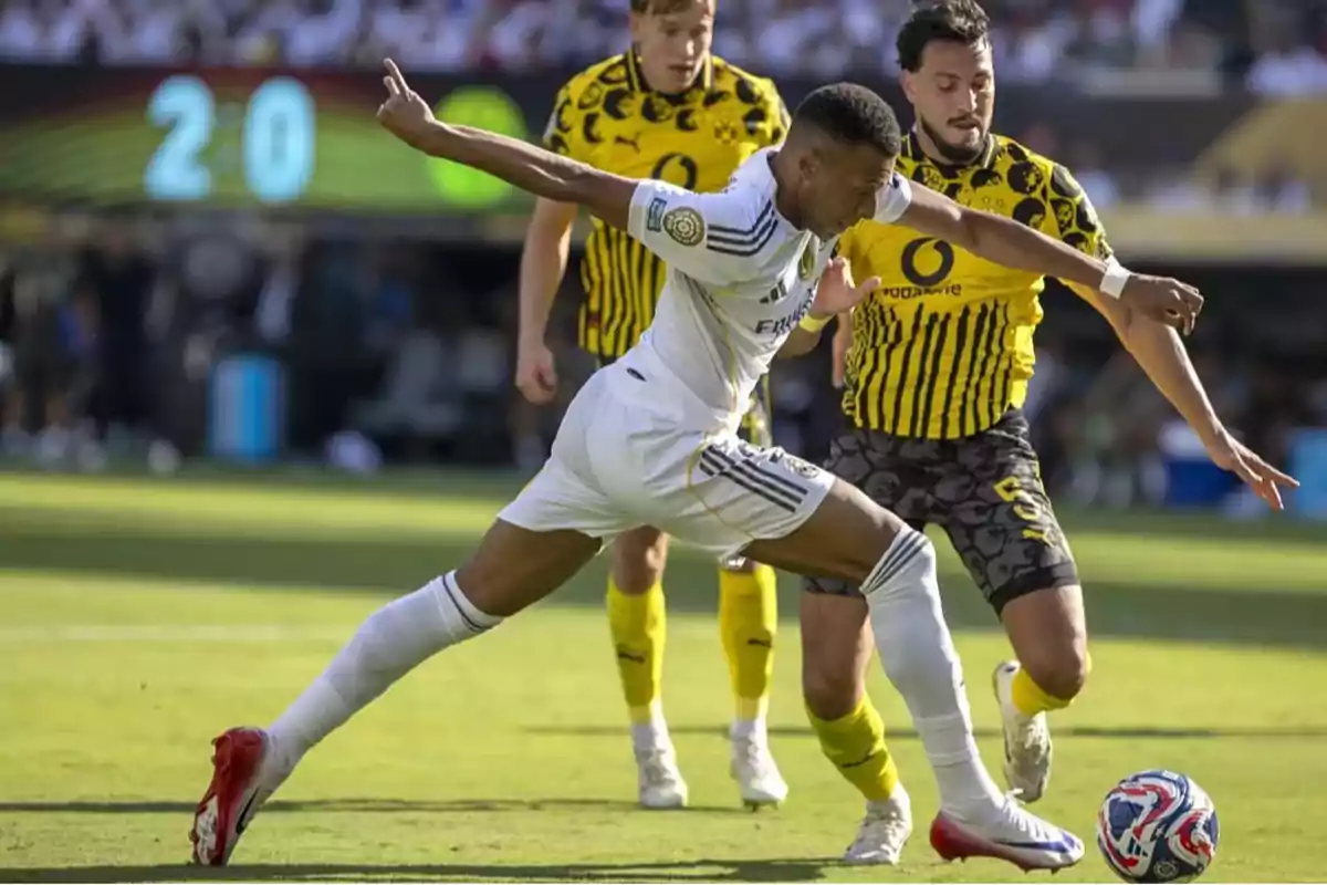 Jugador de fútbol con uniforme blanco intenta controlar el balón mientras es presionado por un rival con uniforme amarillo y negro durante un partido en un estadio lleno Jugador de fútbol con uniforme blanco intenta controlar el balón mientras es presionado por un rival con uniforme amarillo y negro durante un partido en un estadio lleno