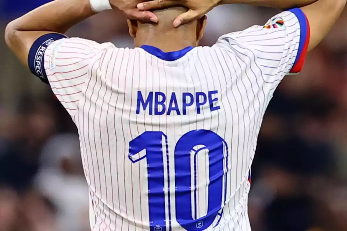 Soccer player wearing the number 10 jersey with the name Mbappé visible from the back, hands on his head in frustration. Soccer player wearing the number 10 jersey with the name Mbappé visible from the back, hands on his head in frustration.