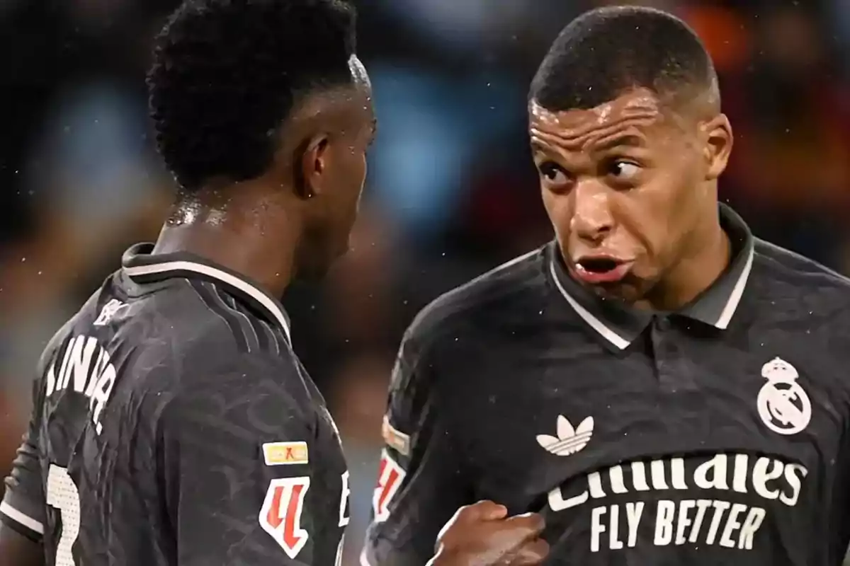 Dos futbolistas del Real Madrid conversan intensamente en el campo durante un partido, ambos llevan uniforme negro y uno de ellos gesticula de manera expresiva.