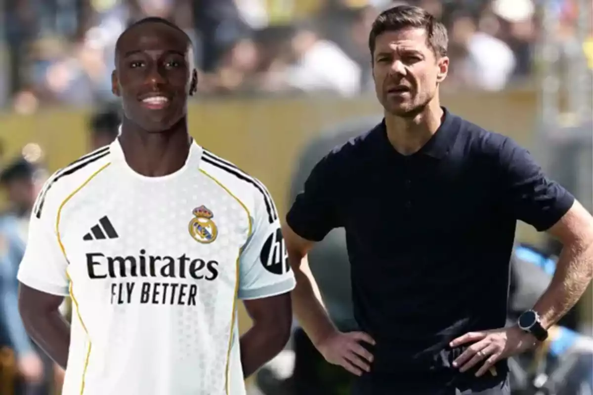 Un futbolista con el uniforme del Real Madrid está de pie junto a un hombre con camiseta oscura que parece ser entrenador en un entorno deportivo.