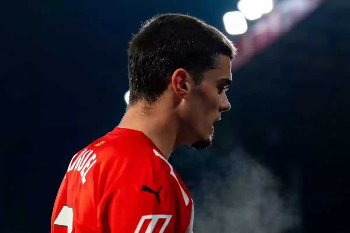 Jugador de fútbol con camiseta roja exhalando vapor en un ambiente frío bajo luces de estadio Jugador de fútbol con camiseta roja exhalando vapor en un ambiente frío bajo luces de estadio