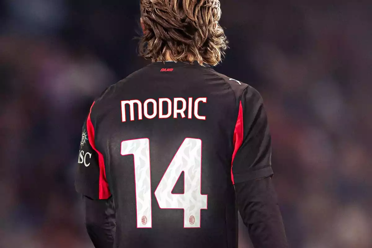 Jugador de fútbol visto de espaldas con el nombre Modric y el número 14 en la camiseta negra con detalles rojos. Jugador de fútbol visto de espaldas con el nombre Modric y el número 14 en la camiseta negra con detalles rojos.