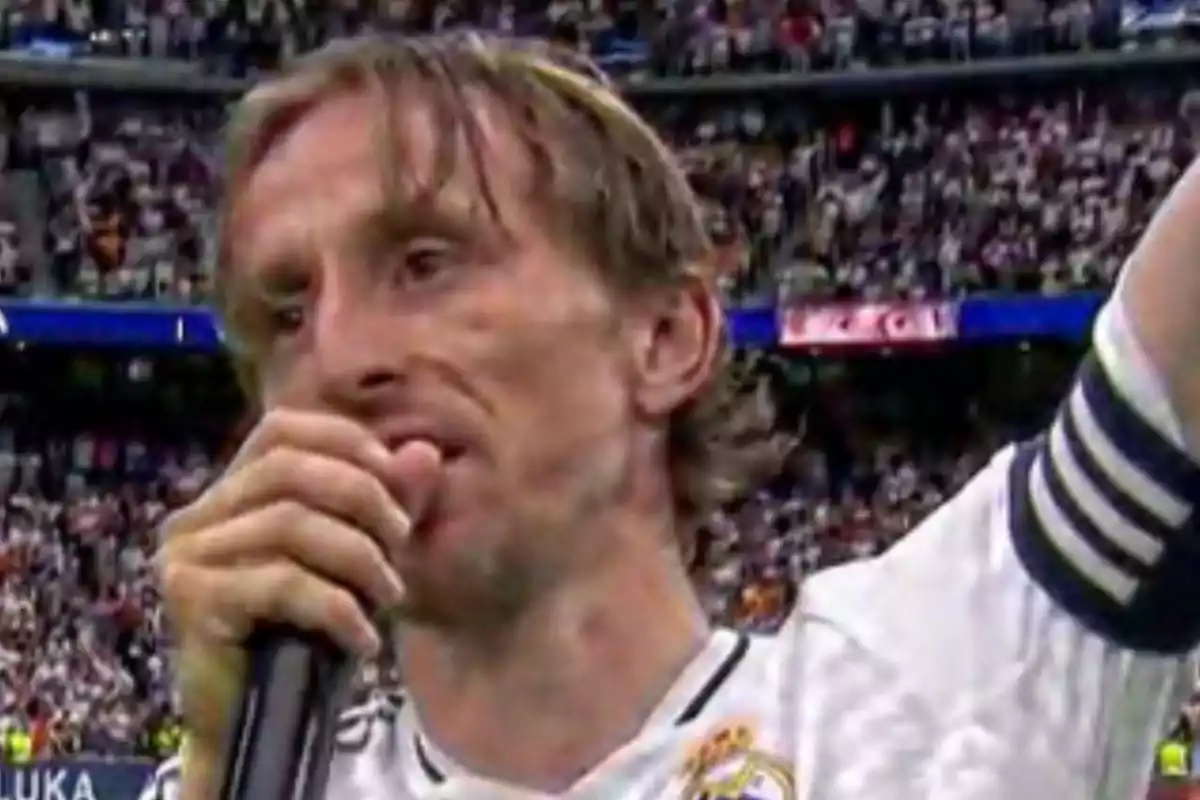 Futbolista con uniforme blanco y brazalete de capitán hablando al micrófono en un estadio lleno de aficionados
