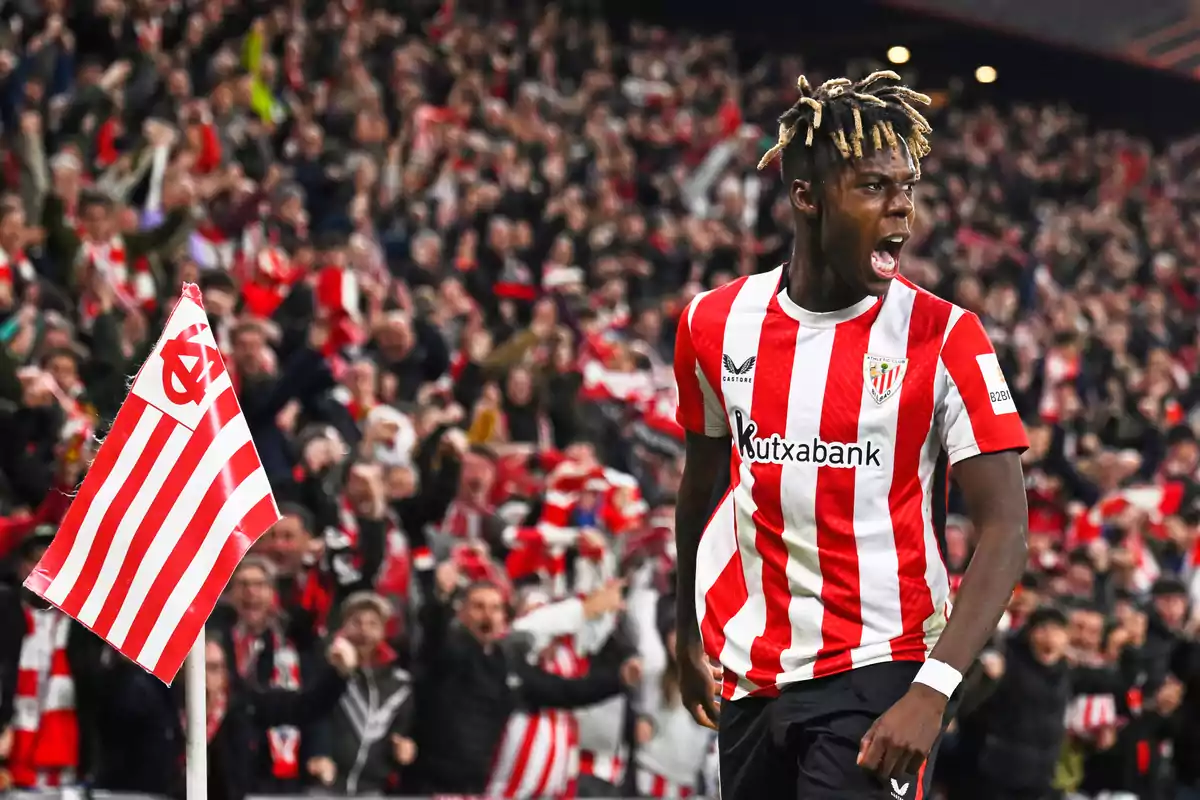 Futbolista del Athletic Club celebrando un gol junto al banderín de córner con la afición animando en el estadio Futbolista del Athletic Club celebrando un gol junto al banderín de córner con la afición animando en el estadio