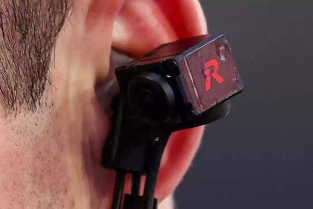 Cámara pequeña colocada sobre la oreja de una persona con la letra R en rojo en el costado del dispositivo Cámara pequeña colocada sobre la oreja de una persona con la letra R en rojo en el costado del dispositivo