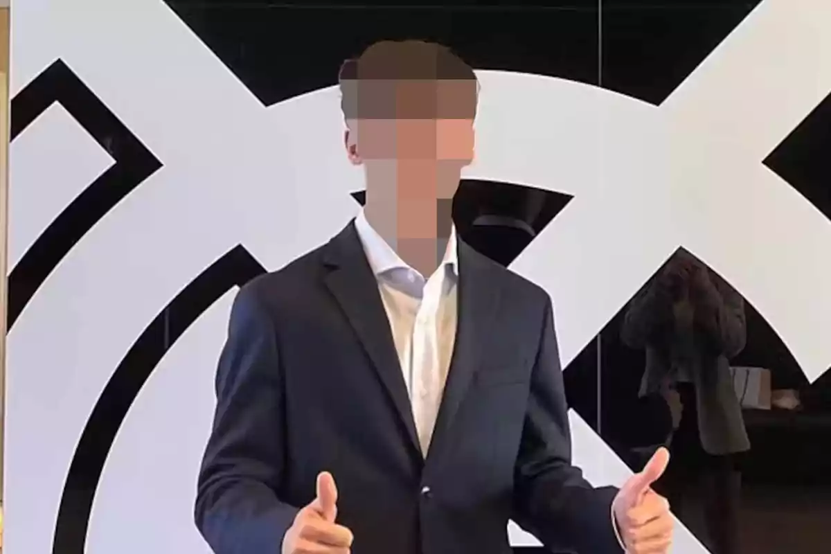 Persona con el rostro pixelado usando traje oscuro y camisa blanca, posando con ambos pulgares arriba frente a un fondo con diseño geométrico en blanco y negro