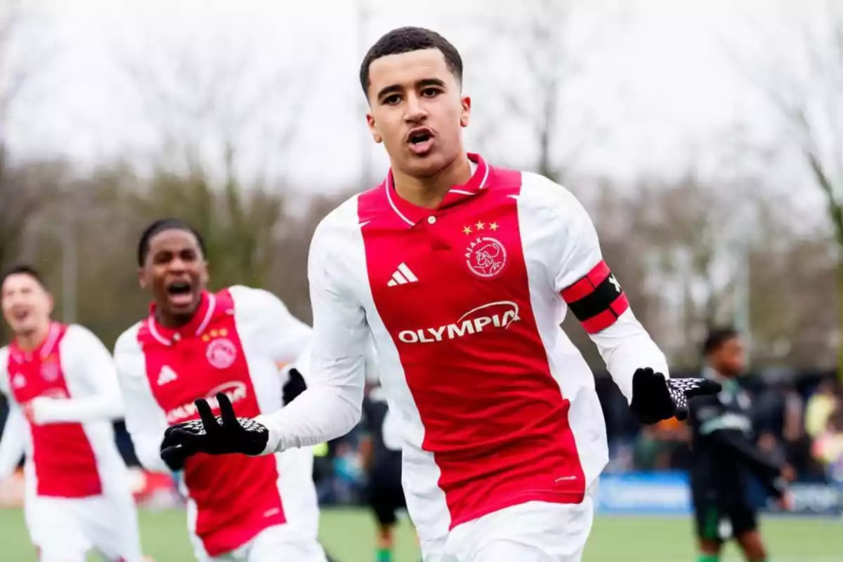 Jugador de fútbol con uniforme del Ajax celebrando un gol en el campo mientras sus compañeros corren detrás de él Jugador de fútbol con uniforme del Ajax celebrando un gol en el campo mientras sus compañeros corren detrás de él