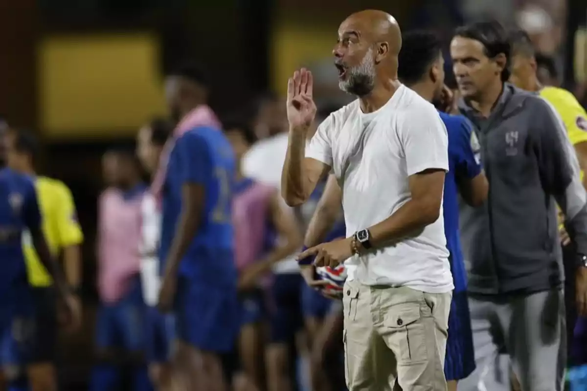 Entrenador de fútbol dando indicaciones en la banda durante un partido con jugadores y cuerpo técnico al fondo Entrenador de fútbol dando indicaciones en la banda durante un partido con jugadores y cuerpo técnico al fondo