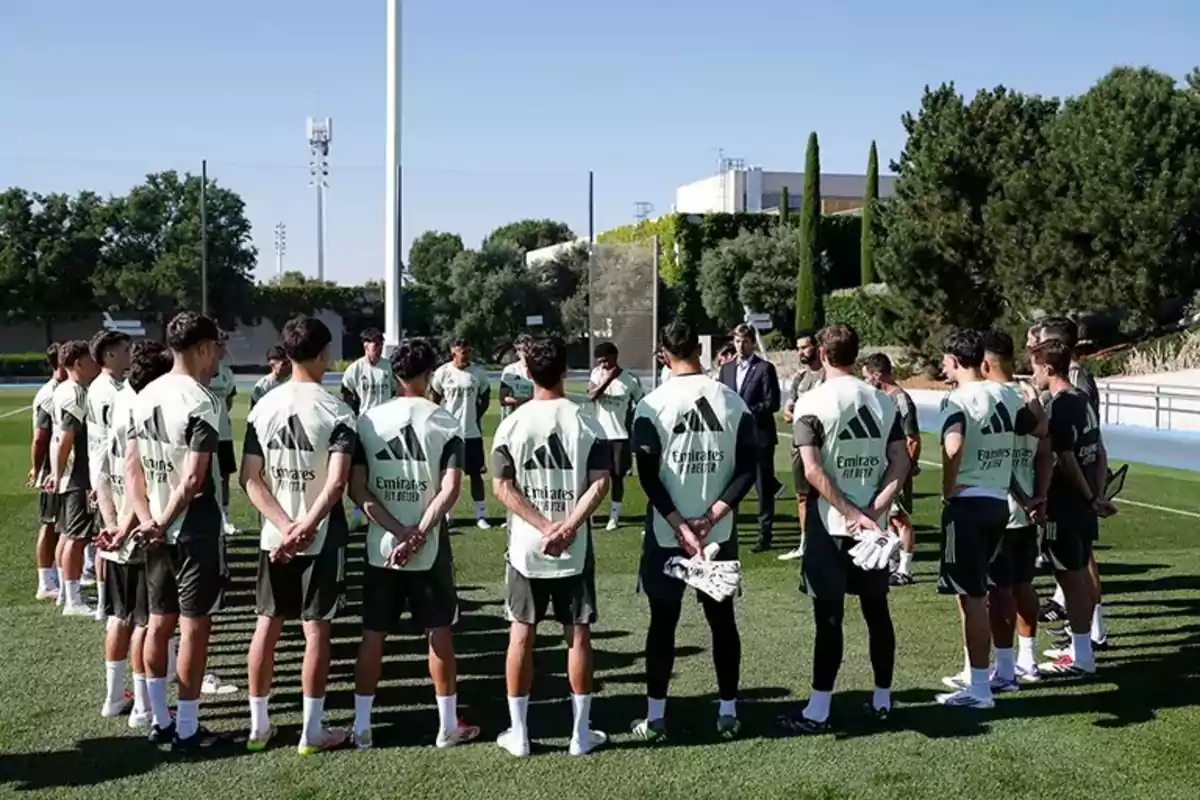 Jugadores de fútbol reunidos en círculo en un campo de entrenamiento escuchando a su entrenador en un día soleado