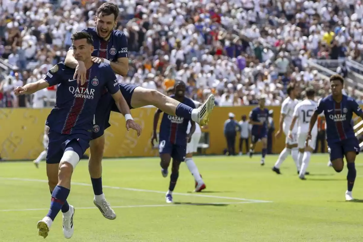 Dos jugadores de fútbol del PSG celebran un gol en el campo mientras sus compañeros corren hacia ellos y el público llena las gradas. Dos jugadores de fútbol del PSG celebran un gol en el campo mientras sus compañeros corren hacia ellos y el público llena las gradas.