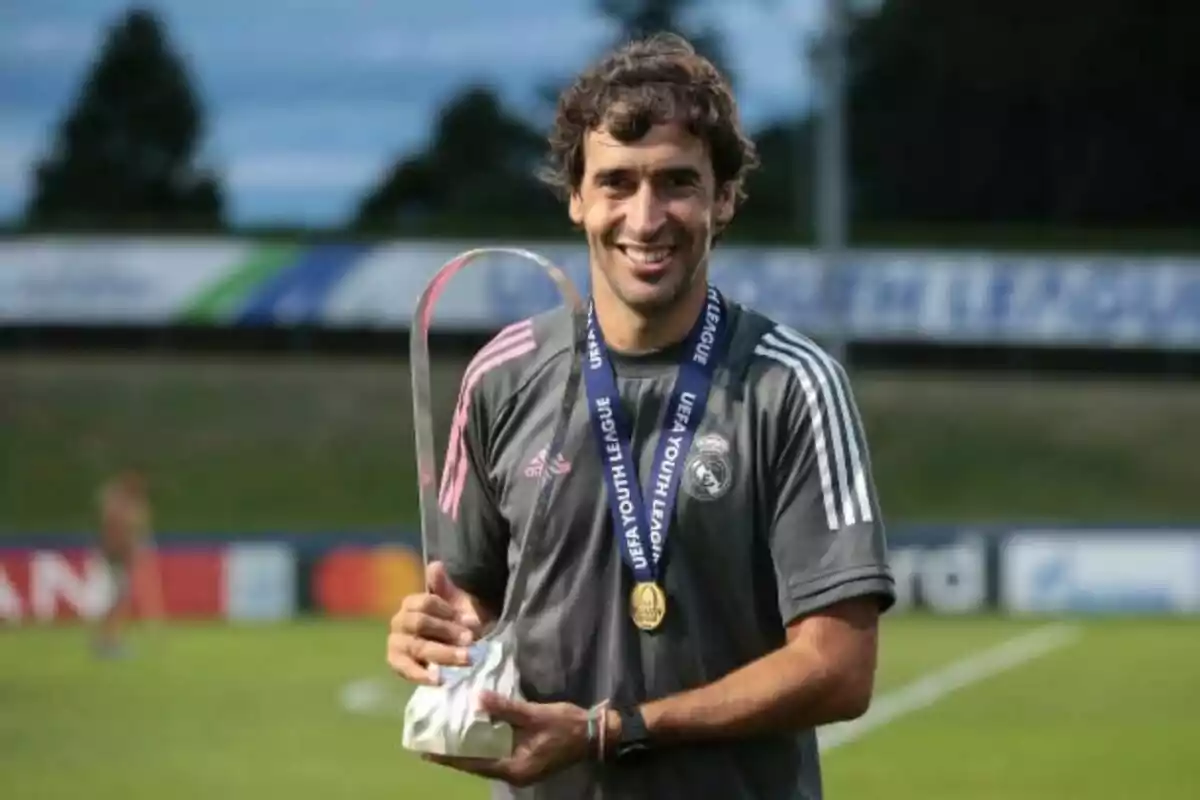 Smiling man in a gray sports jersey and medal, holding a trophy on a soccer field Smiling man in a gray sports jersey and medal, holding a trophy on a soccer field
