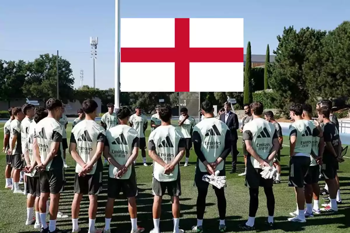Jugadores de fútbol reunidos en círculo en un campo de entrenamiento con una gran bandera de Inglaterra al fondo