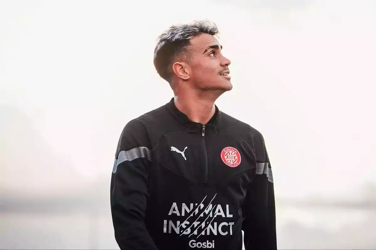 Futbolista con uniforme negro del Girona FC mirando hacia arriba sobre un fondo claro Futbolista con uniforme negro del Girona FC mirando hacia arriba sobre un fondo claro